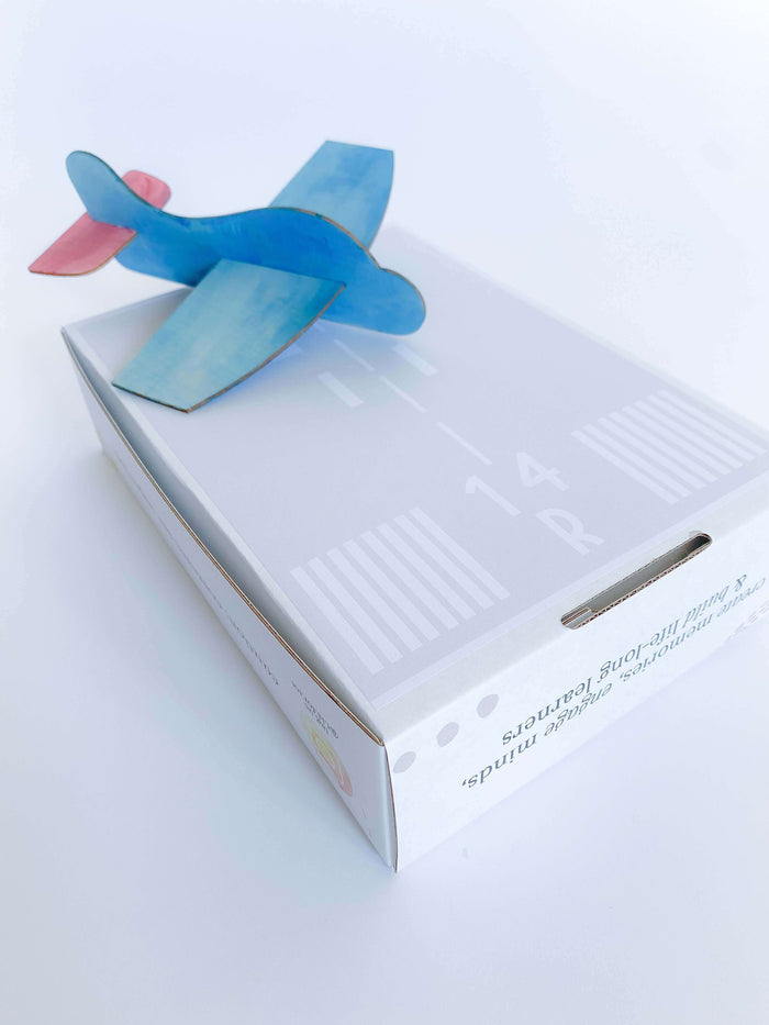 Airplane play and learn kit for kids, offering supplies to create and race four different airplanes. Includes wooden airplane craft, paper airplane, straw airplane, position words playdough mats, and a children's book on airplanes.