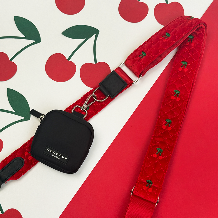 Cherry Velvet Crush bag strap with black dog walking bag on a red background with cherry print.