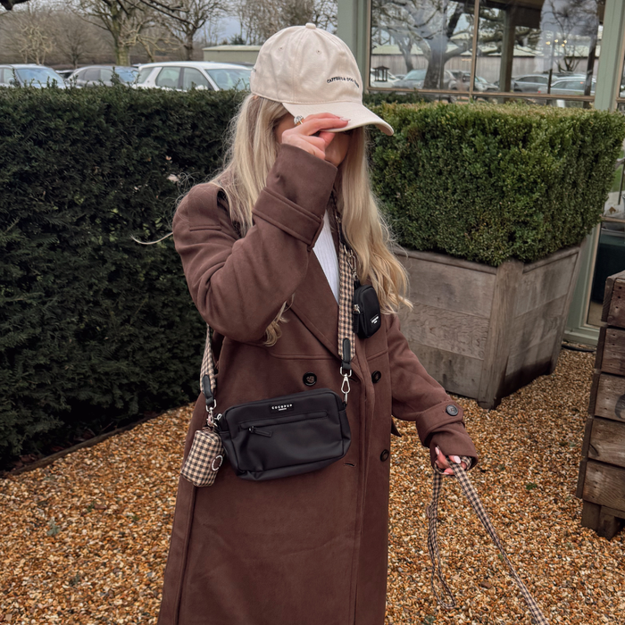 Woman in brown coat and cap holds leash with Cocopup London bag strap in tan and cream Cotswold check pattern.