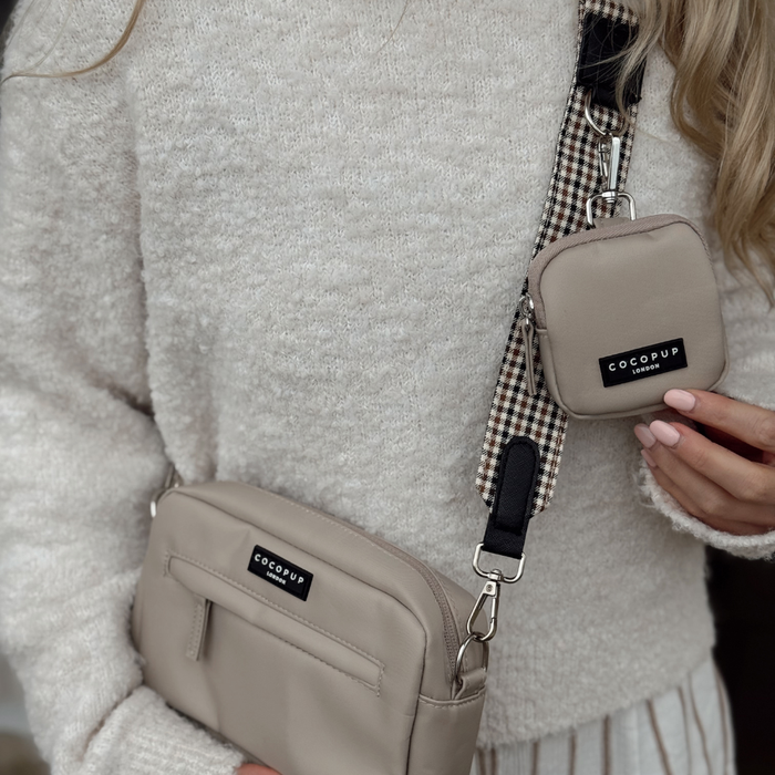 Woman in a cream sweater holds a beige Cocopup London bag with Heritage Check strap and matching pouch.
