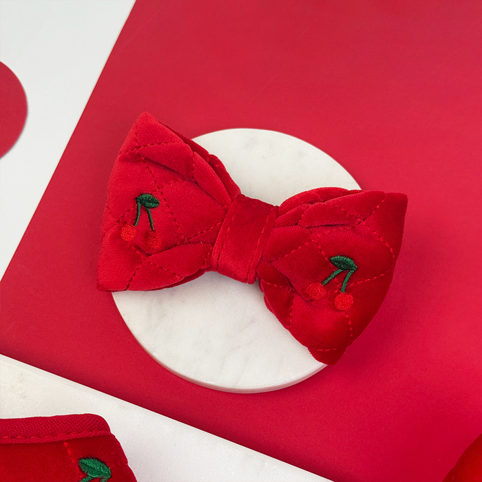 Red and white bow tie with quilted velvet texture and embroidered cherry details.