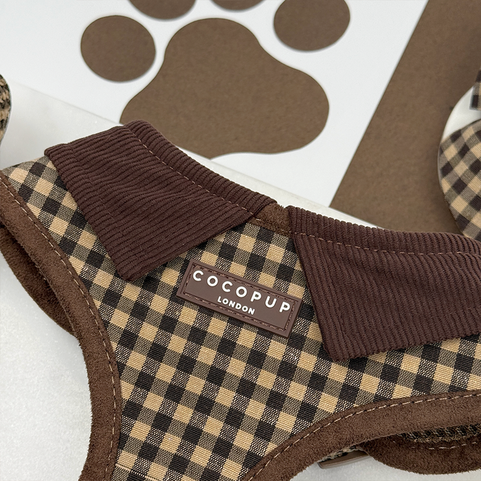 Brown and cream check dog harness with adjustable neck and corduroy collar, shown near a paw print cutout.
