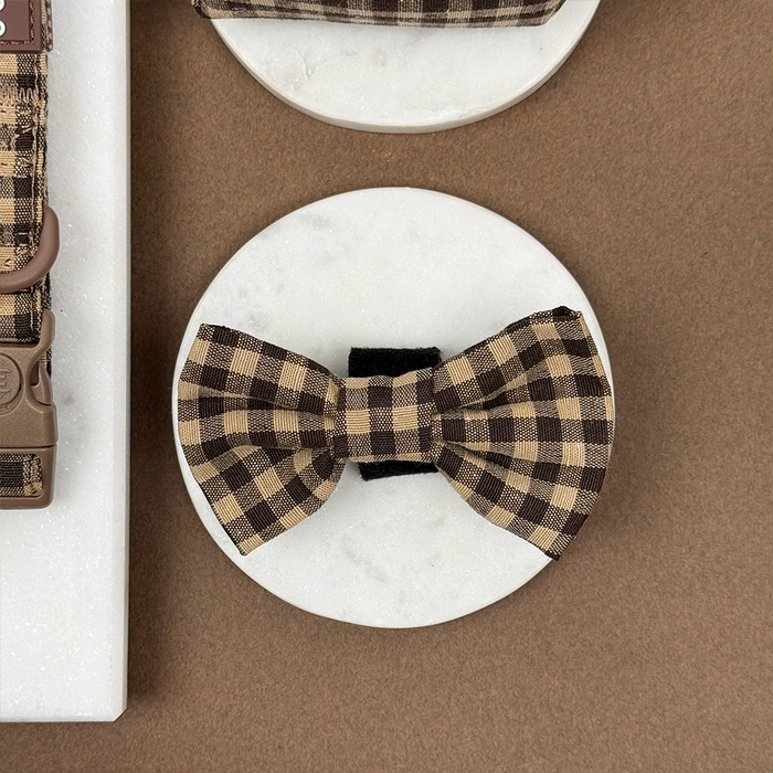 Cocopup London Cotswold Check dog bow tie in a checked pattern, displayed on white marble with a soft countryside backdrop.