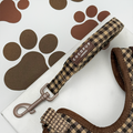 Brown check Cocopup London dog lead on a brown surface with paw prints.