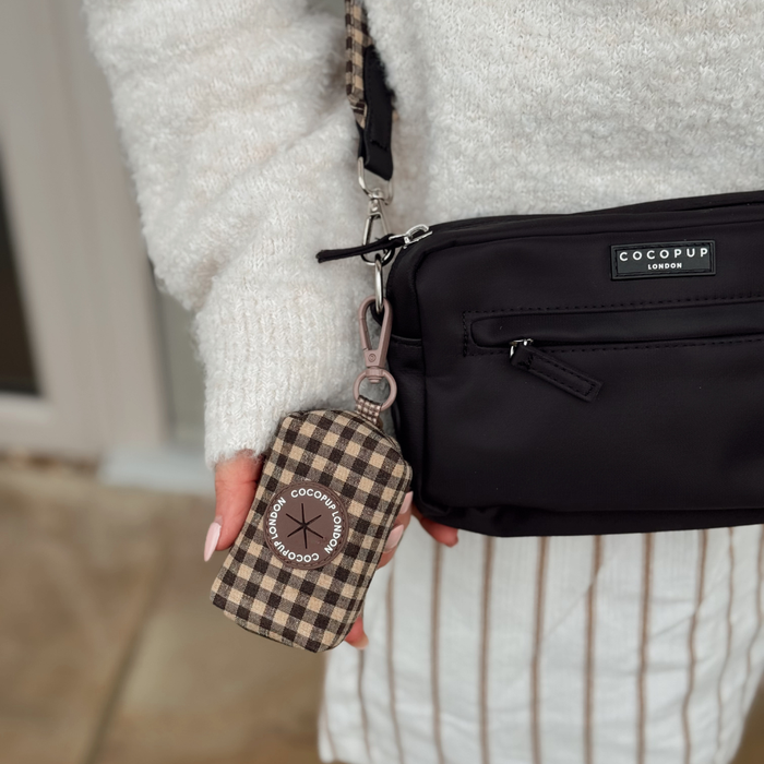 Person in a white sweater and striped pants holds a Cocopup London bag with a plaid Cotswold Check poop bag holder attached.