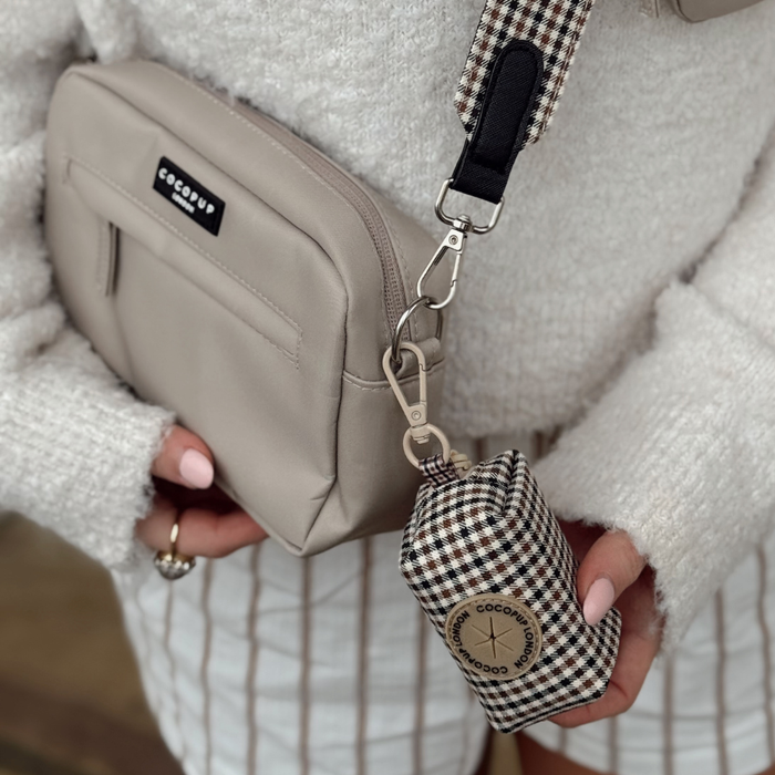 Woman in a white sweater and striped skirt holds a beige checked Cocopup London poop bag holder.