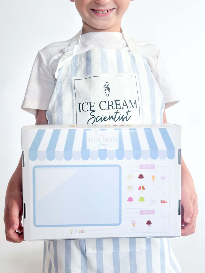 Child wearing an 'Ice Cream Scientist' apron holding an ice cream kit with colorful graphics.