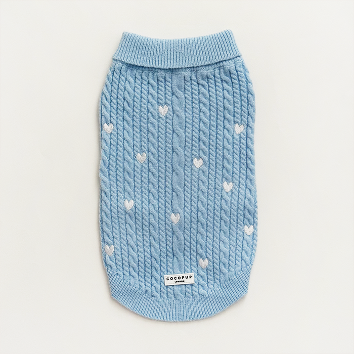 Light blue cable knit dog sweater featuring white heart pattern and a branded label on the front.