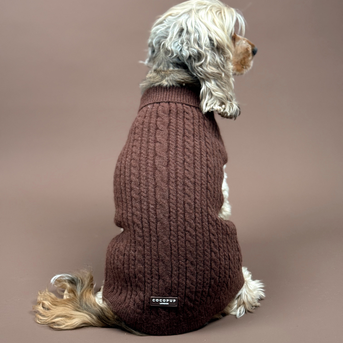Dog wearing a brown cable knit Cocopup London jumper, sitting on a matching brown background, facing away.