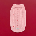 Pink cable knit Cocopup London jumper with heart pattern, displayed on a red background decorated with small red hearts.
