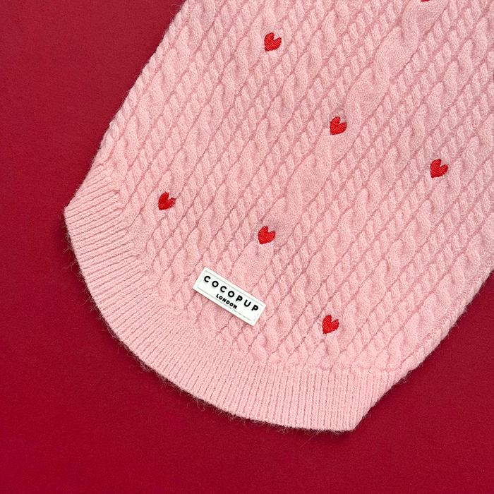 Pink cable knit jumper with red heart pattern, from Cocopup London, displayed on a vibrant red background.
