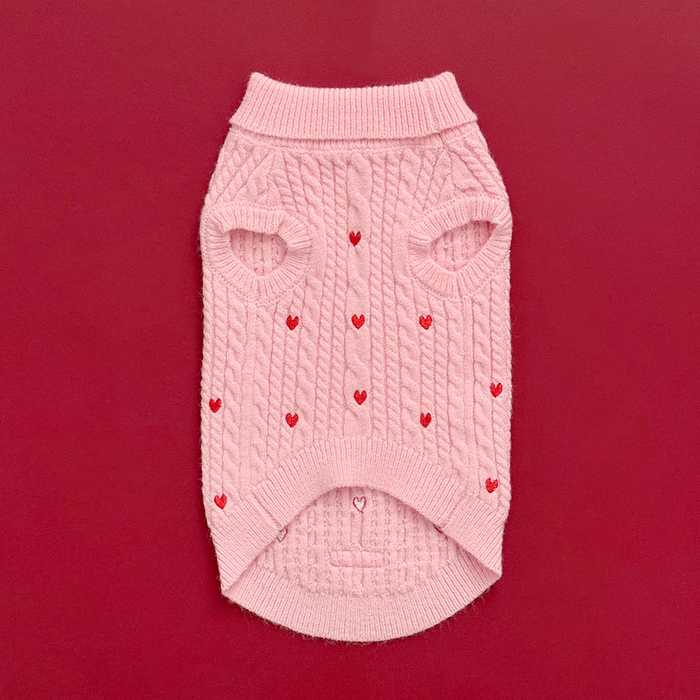 Pink cable knit Cocopup London jumper with heart pattern, laid flat on a red background.