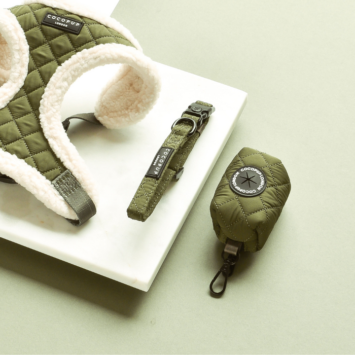Khaki quilted poop bag holder with olive green quilted dog harness and collar on a white marble surface.