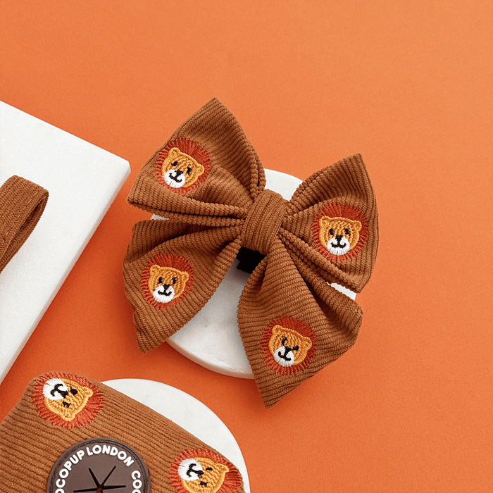 A brown / orange corduroy dog sailor bow tie with embroidered lion faces. With velcro attachment.