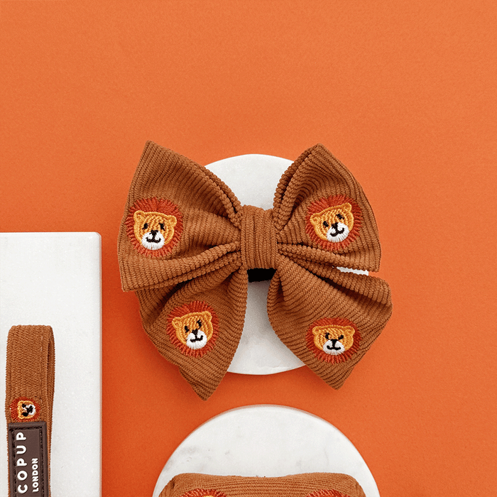 A brown / orange corduroy dog sailor bow tie with embroidered lion faces. With velcro attachment.