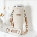 Cream quilted tumbler carry case with beige strap, displayed on a white shelf next to a vase.