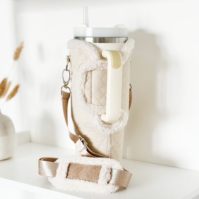 Cream quilted tumbler carry case with straw tumbler inside, displayed on a white shelf.