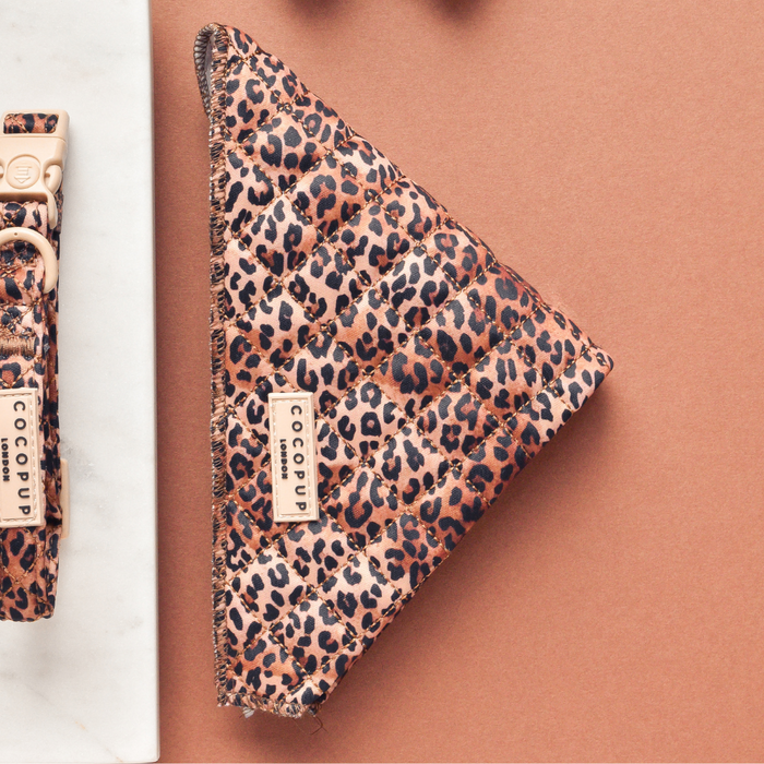 Quilted leopard print dog bandana with a Cocopup London label, displayed on a brown background.