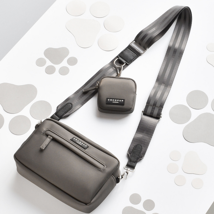Mocha reflective bag strap by Cocopup London attached to a gray crossbody bag with small pouch on paw-print background.