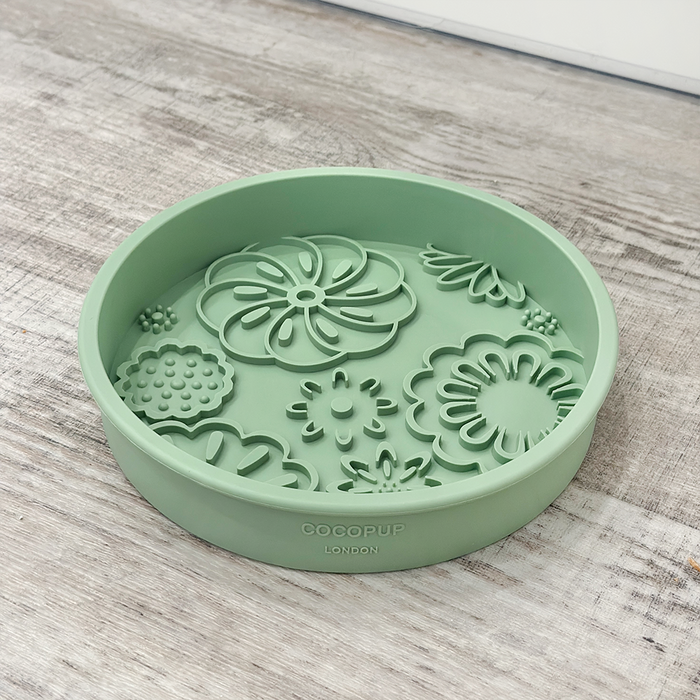 Sage green slow feeder dog bowl with raised floral patterns, displayed on a wooden surface.