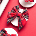 Tartan-patterned sailor bow tie by Cocopup London displayed on a white card with other bows on a red background.