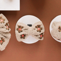 Fuzzy beige teddy bow tie with pink hearts, embroidered, displayed on a round white card.