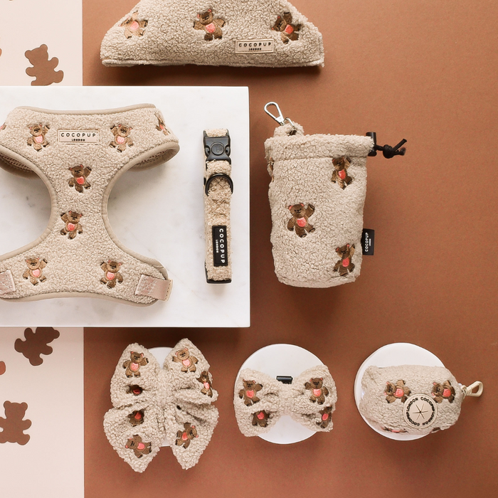Tan dog accessories set with teddy bear pattern, including poop bag holder, harness, bow ties, collar and leash.