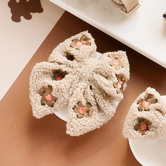 Beige sailor bow tie with embroidered teddy bear faces, displayed on a white dish.