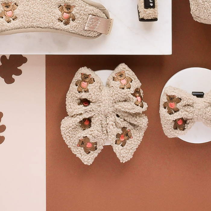 Cream fluffy slides and a beige embroidered sailor bow tie displayed on a brown and white surface.