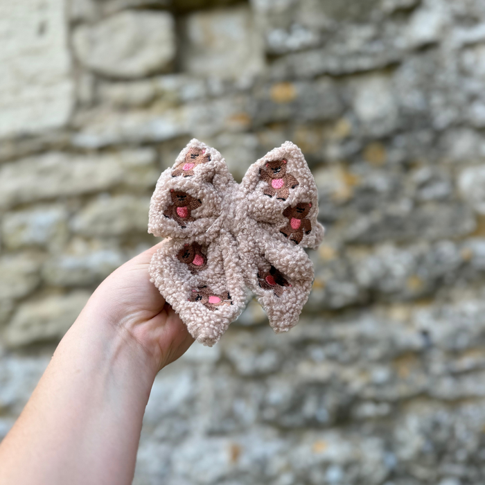 Hand holding a beige, brown, and pink embroidered teddy sailor bow tie by Cocopup London.